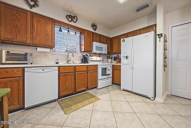 kitchen featuring sink, light tile patterned flooring, white appliances, and a textured ceiling