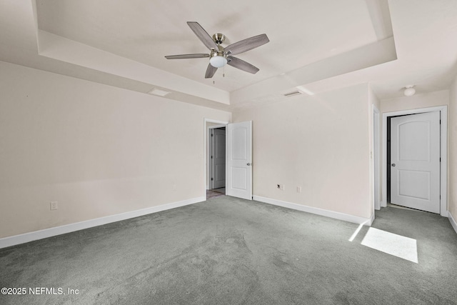 empty room with ceiling fan, a tray ceiling, and carpet floors