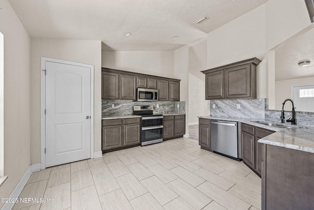 kitchen featuring light stone counters, dark brown cabinetry, stainless steel appliances, and sink