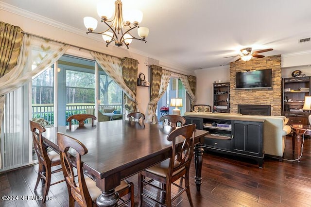 dining space featuring ceiling fan with notable chandelier, crown molding, dark wood-type flooring, and a stone fireplace