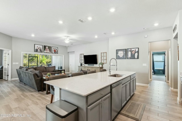 kitchen with sink, light hardwood / wood-style flooring, stainless steel dishwasher, gray cabinets, and a kitchen island with sink