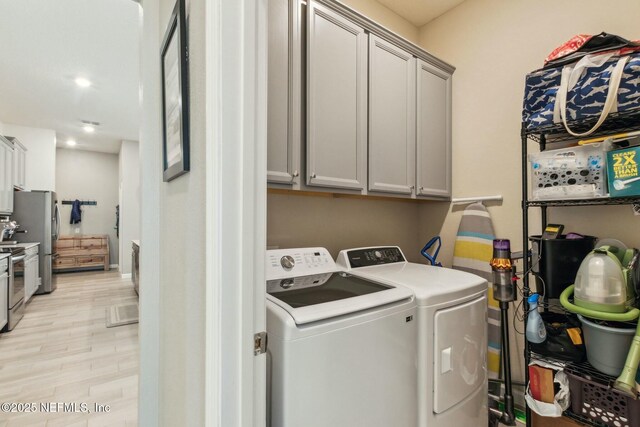 washroom featuring washing machine and dryer, light hardwood / wood-style floors, and cabinets