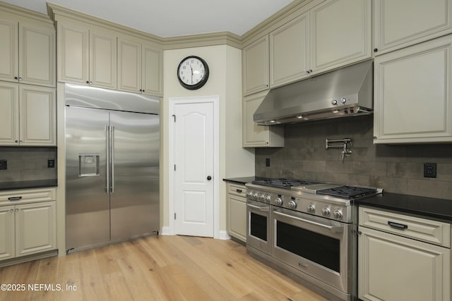 kitchen with tasteful backsplash, light hardwood / wood-style flooring, cream cabinetry, and high quality appliances