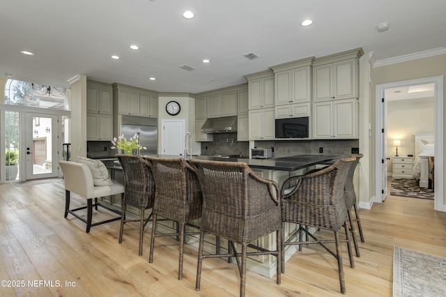 kitchen featuring light hardwood / wood-style flooring, a kitchen bar, built in fridge, backsplash, and ornamental molding