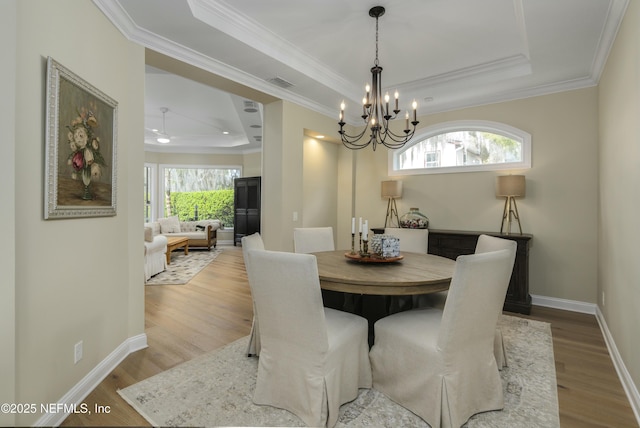 dining space with a notable chandelier, a tray ceiling, crown molding, and light hardwood / wood-style flooring