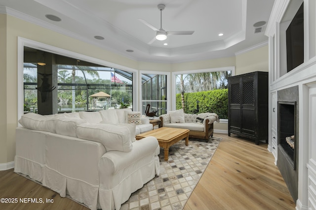 living room featuring a raised ceiling, hardwood / wood-style floors, ceiling fan, ornamental molding, and a premium fireplace