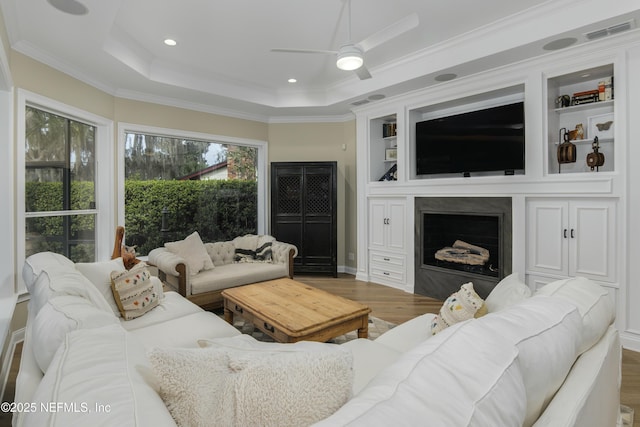 living room featuring hardwood / wood-style flooring, ceiling fan, a tray ceiling, and ornamental molding