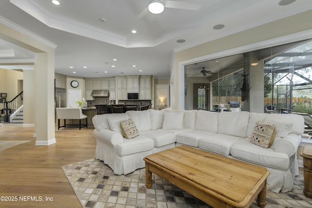 living room featuring light wood-type flooring, ceiling fan, crown molding, and a tray ceiling