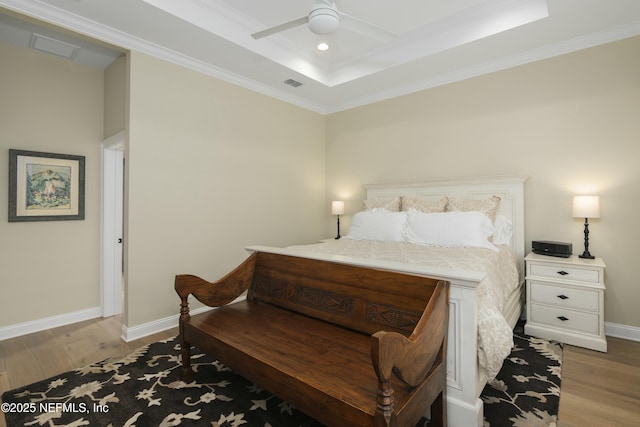 bedroom with ceiling fan, light wood-type flooring, ornamental molding, and a tray ceiling