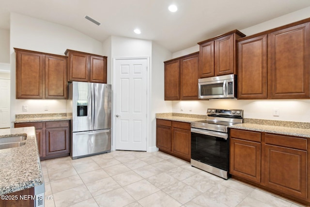 kitchen with vaulted ceiling, light tile patterned floors, appliances with stainless steel finishes, and light stone counters