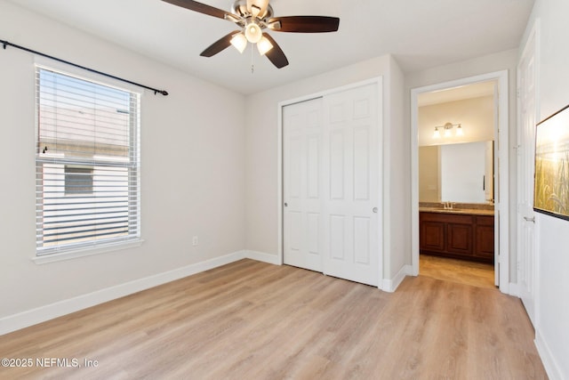 unfurnished bedroom with ceiling fan, sink, light wood-type flooring, connected bathroom, and a closet