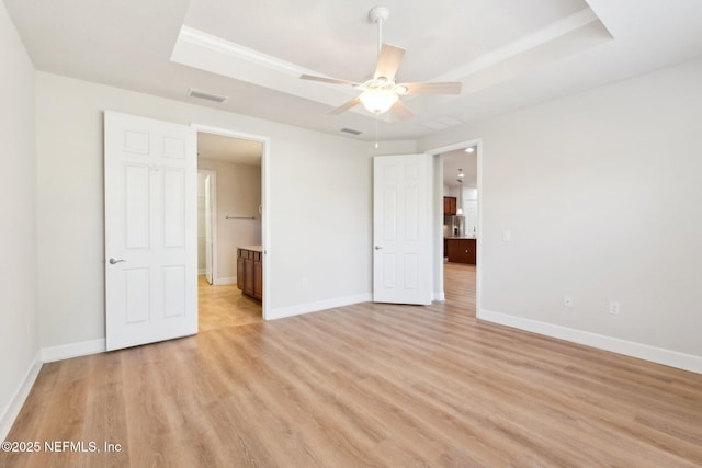 unfurnished bedroom featuring ceiling fan, ensuite bathroom, light hardwood / wood-style flooring, and a raised ceiling