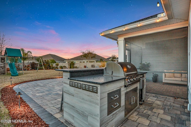 patio terrace at dusk with a playground, a grill, and exterior kitchen