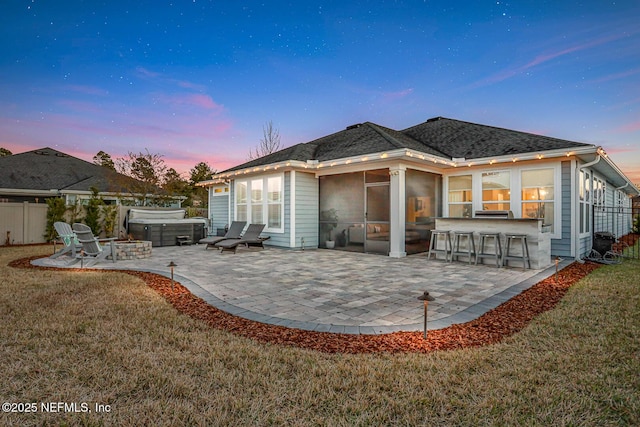 back house at dusk featuring a lawn, a hot tub, a patio area, and an outdoor bar