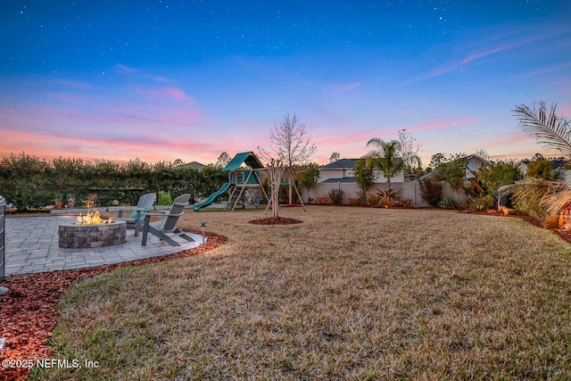 yard at dusk with a playground, a patio area, and a fire pit