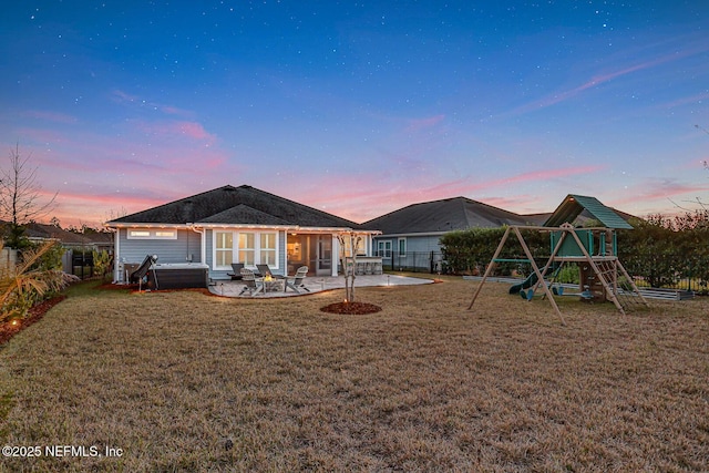 back house at dusk with a lawn, a patio, and a playground