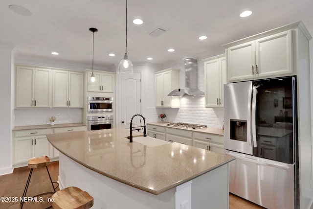 kitchen featuring sink, appliances with stainless steel finishes, wall chimney exhaust hood, and a kitchen island with sink