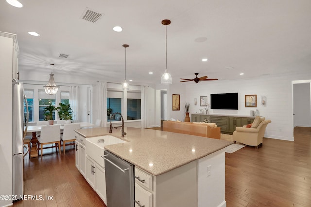 kitchen with white cabinets, appliances with stainless steel finishes, sink, hanging light fixtures, and a center island with sink