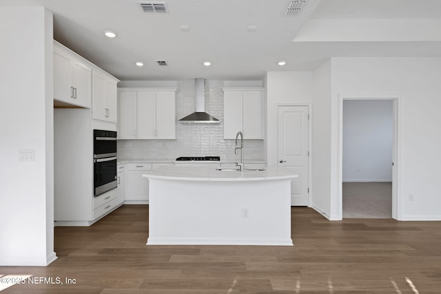 kitchen with wall chimney range hood, sink, white cabinets, and a center island with sink