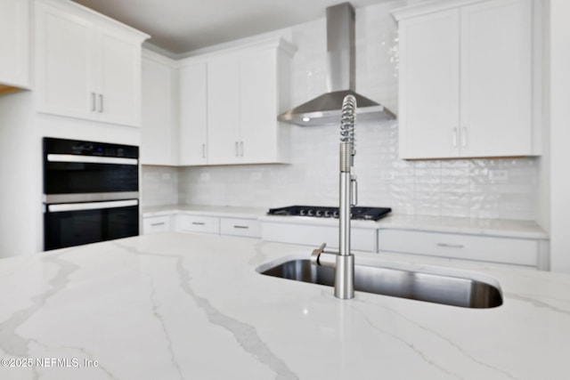 kitchen featuring white cabinetry, wall chimney range hood, light stone counters, and black appliances