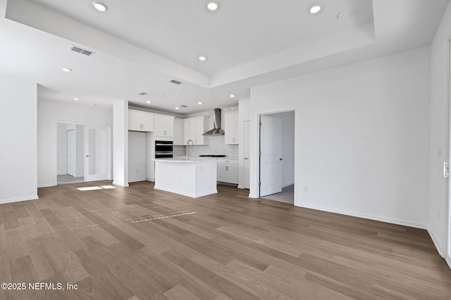 unfurnished living room with sink, a tray ceiling, and light hardwood / wood-style flooring