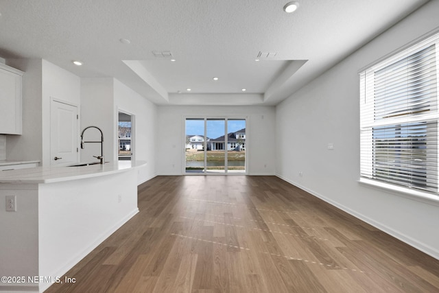 unfurnished living room featuring wood-type flooring, a tray ceiling, sink, and a textured ceiling