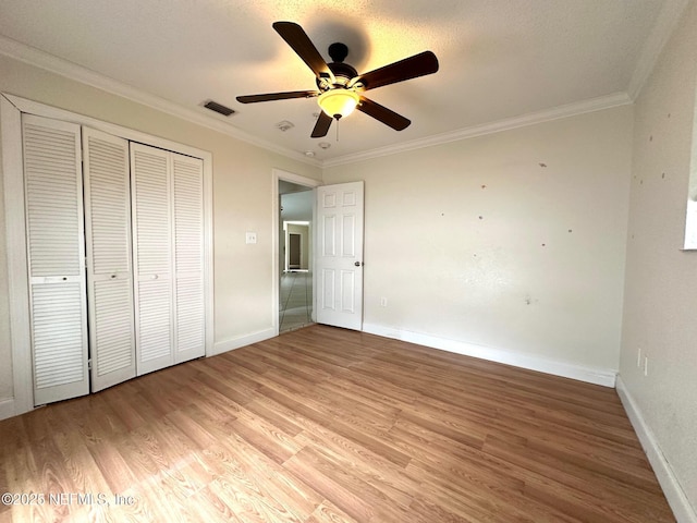 unfurnished bedroom with ceiling fan, crown molding, light hardwood / wood-style floors, and a closet