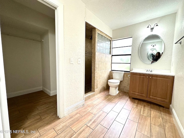 bathroom with a textured ceiling, toilet, a shower, and vanity