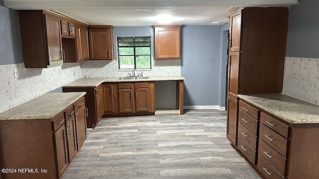 kitchen with sink, tasteful backsplash, light wood-type flooring, and light stone countertops