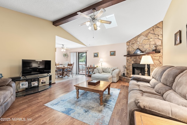 living room featuring vaulted ceiling with skylight, a textured ceiling, wood-type flooring, a fireplace, and ceiling fan