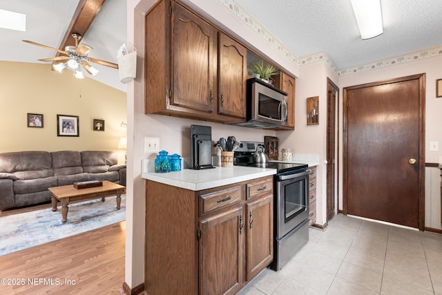 kitchen featuring light tile patterned floors, ceiling fan, stainless steel appliances, a textured ceiling, and vaulted ceiling