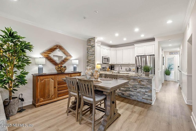 kitchen with appliances with stainless steel finishes, light stone counters, white cabinets, light wood-type flooring, and kitchen peninsula