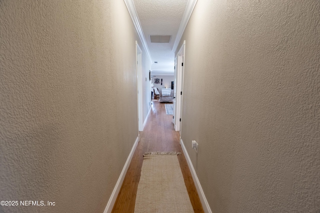 corridor with a textured ceiling, ornamental molding, and hardwood / wood-style floors