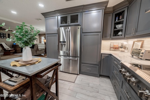 kitchen with tasteful backsplash, stove, stainless steel refrigerator with ice dispenser, gray cabinetry, and a textured ceiling