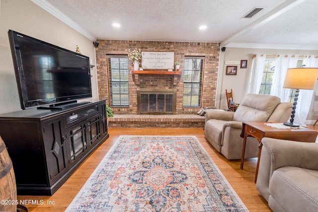 living room featuring a fireplace, light wood-type flooring, a textured ceiling, ornamental molding, and brick wall