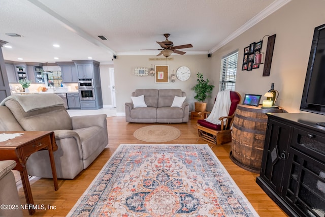 living room with light hardwood / wood-style floors, a textured ceiling, ornamental molding, and ceiling fan