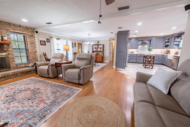 living room featuring a textured ceiling, an inviting chandelier, a fireplace, light wood-type flooring, and crown molding