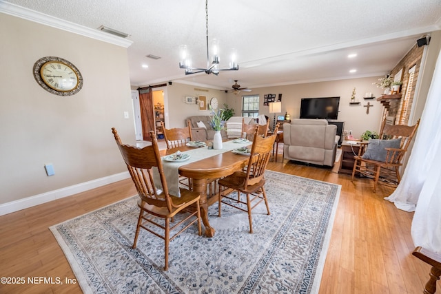 dining area featuring light wood-type flooring, ceiling fan with notable chandelier, ornamental molding, and a barn door