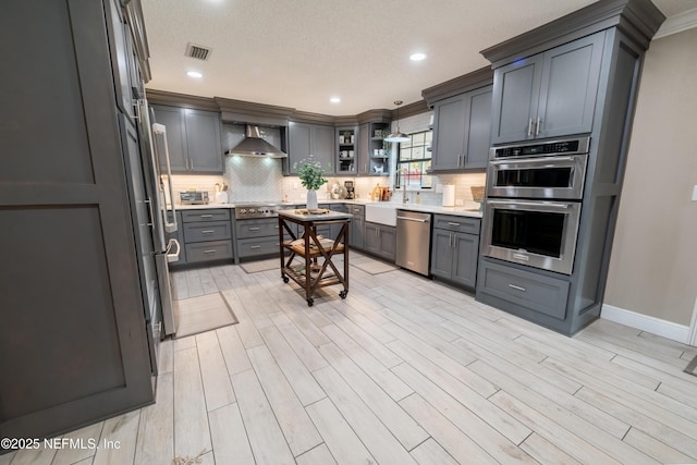 kitchen with hanging light fixtures, wall chimney exhaust hood, gray cabinets, and stainless steel appliances