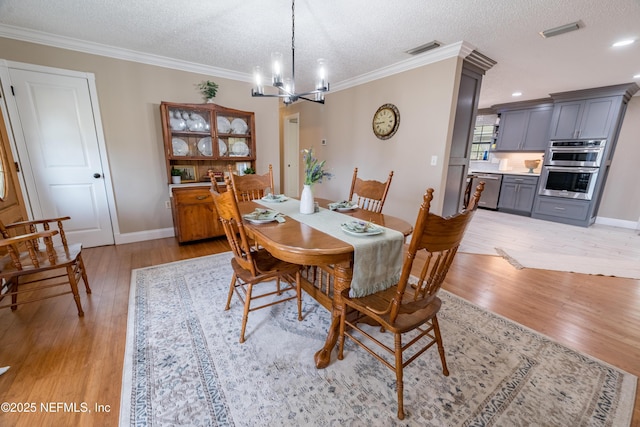 dining space with a textured ceiling, crown molding, light hardwood / wood-style floors, and a notable chandelier