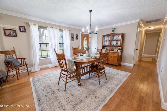 dining room featuring light hardwood / wood-style floors, a textured ceiling, ornamental molding, and an inviting chandelier