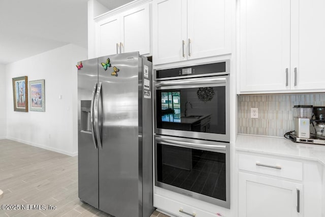 kitchen featuring stainless steel appliances, white cabinets, light stone counters, light hardwood / wood-style floors, and backsplash