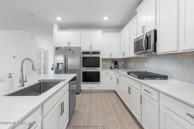 kitchen featuring stainless steel appliances, light stone countertops, white cabinets, and sink