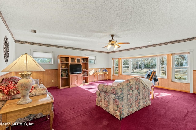 carpeted living room featuring a textured ceiling, ceiling fan, a wealth of natural light, and wooden walls