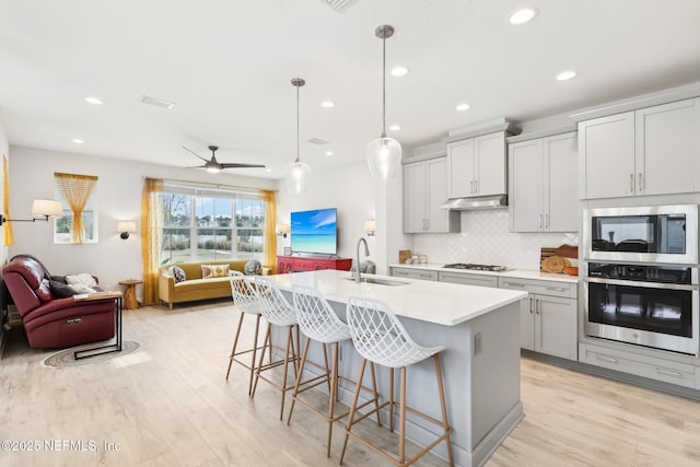 kitchen with an island with sink, ceiling fan, stainless steel appliances, decorative light fixtures, and sink