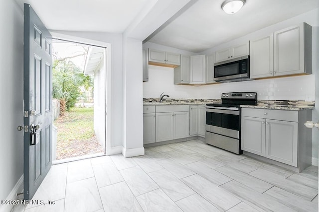 kitchen with sink, stone counters, tasteful backsplash, gray cabinetry, and appliances with stainless steel finishes