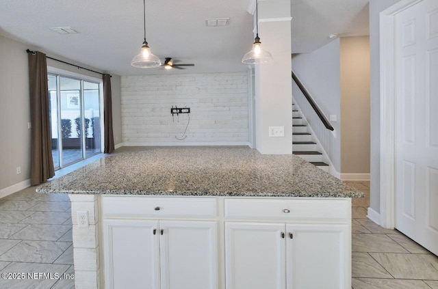 kitchen with stone counters, ceiling fan, pendant lighting, and white cabinetry