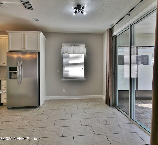 kitchen featuring a textured ceiling, stainless steel fridge, tasteful backsplash, and white cabinetry