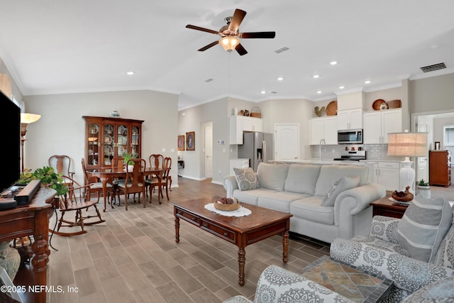 living room featuring light wood-type flooring, lofted ceiling, sink, ornamental molding, and ceiling fan