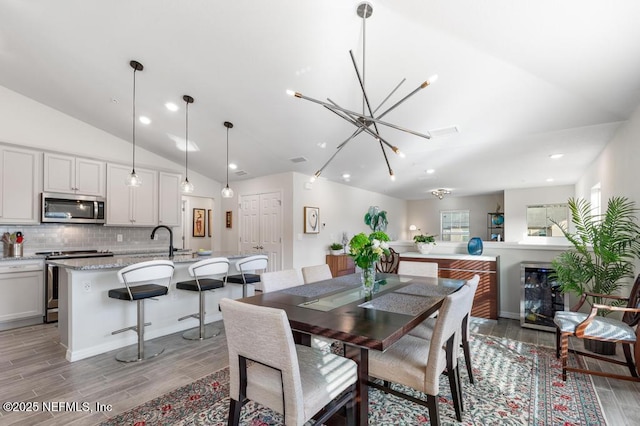 dining area with sink, lofted ceiling, a notable chandelier, and wine cooler